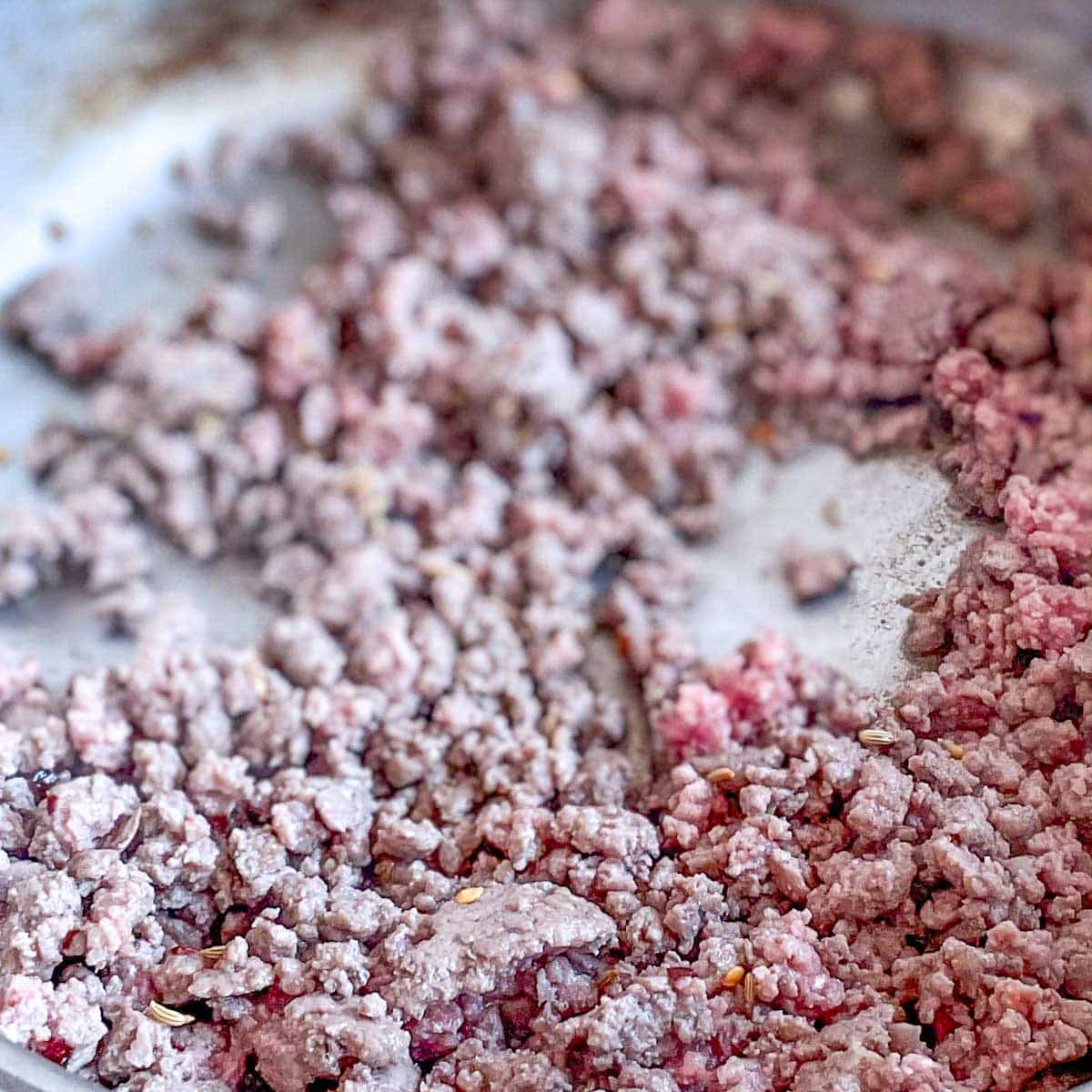 Ground beef is browned in a stainless steel pan.