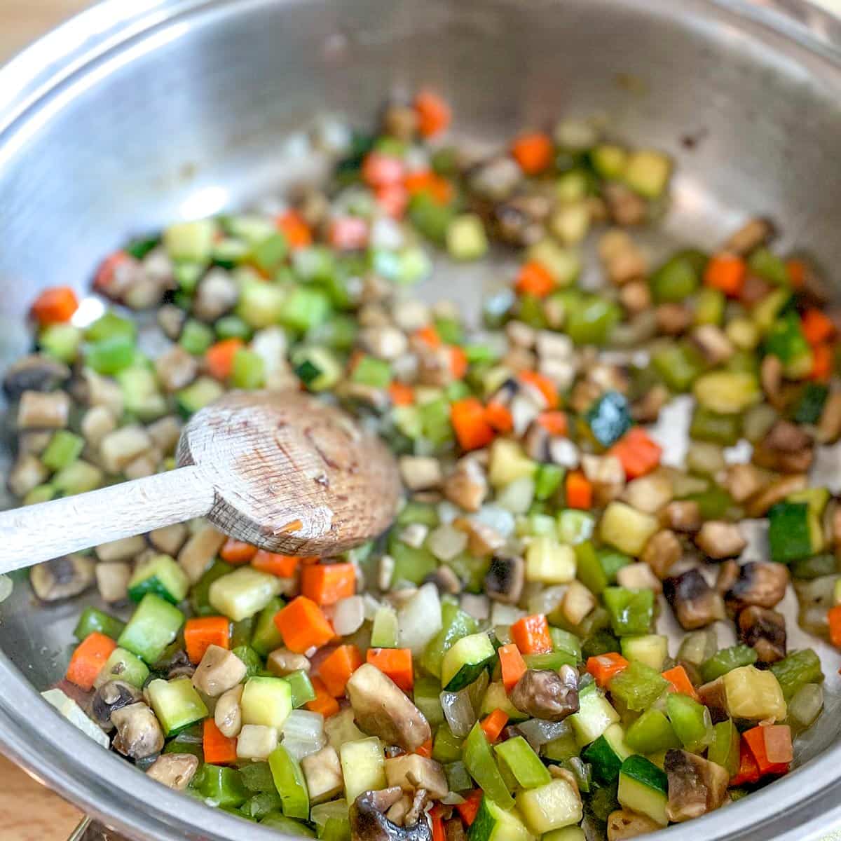 The diced vegetables are sweated in a stainless steel pan.
