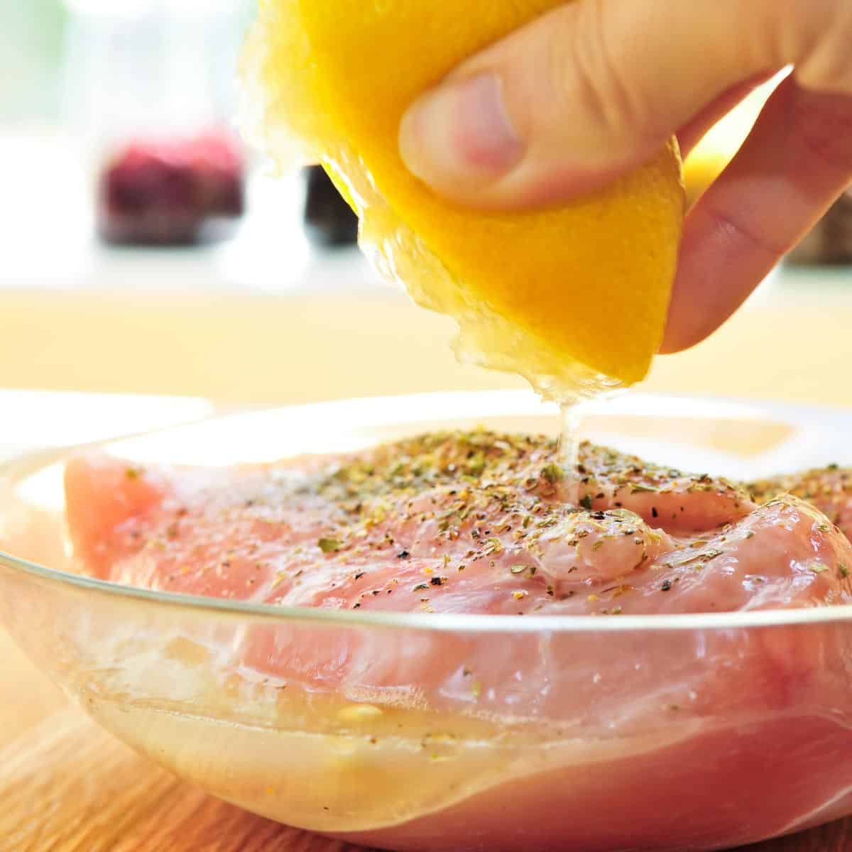 Lemon is squeezed over seasoned chicken in a glass dish.