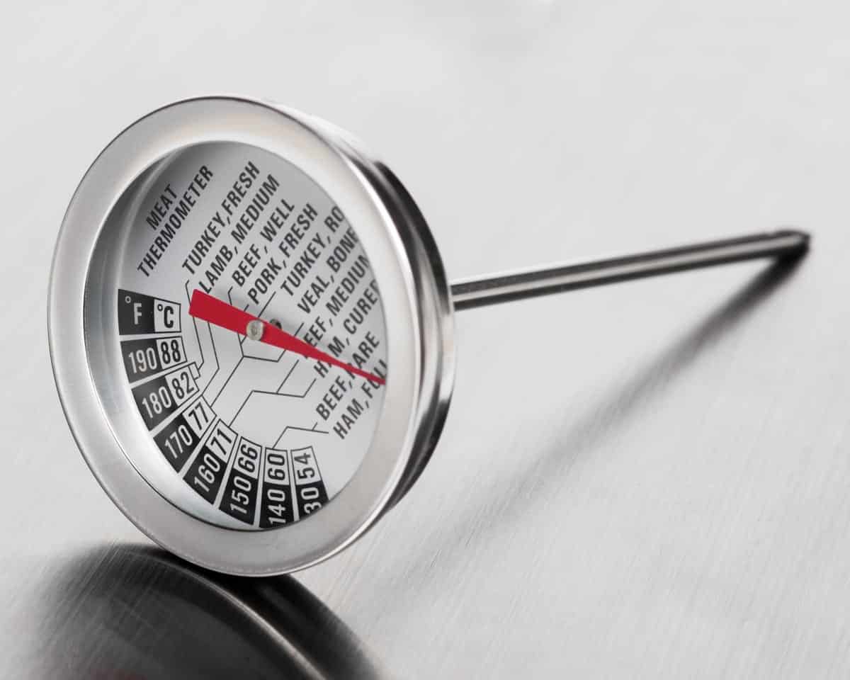 A meat thermometer sits on a stainless steel surface.