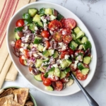 A Mediterranean cucumber tomato salad is shown in a white serving dish with a spoon.