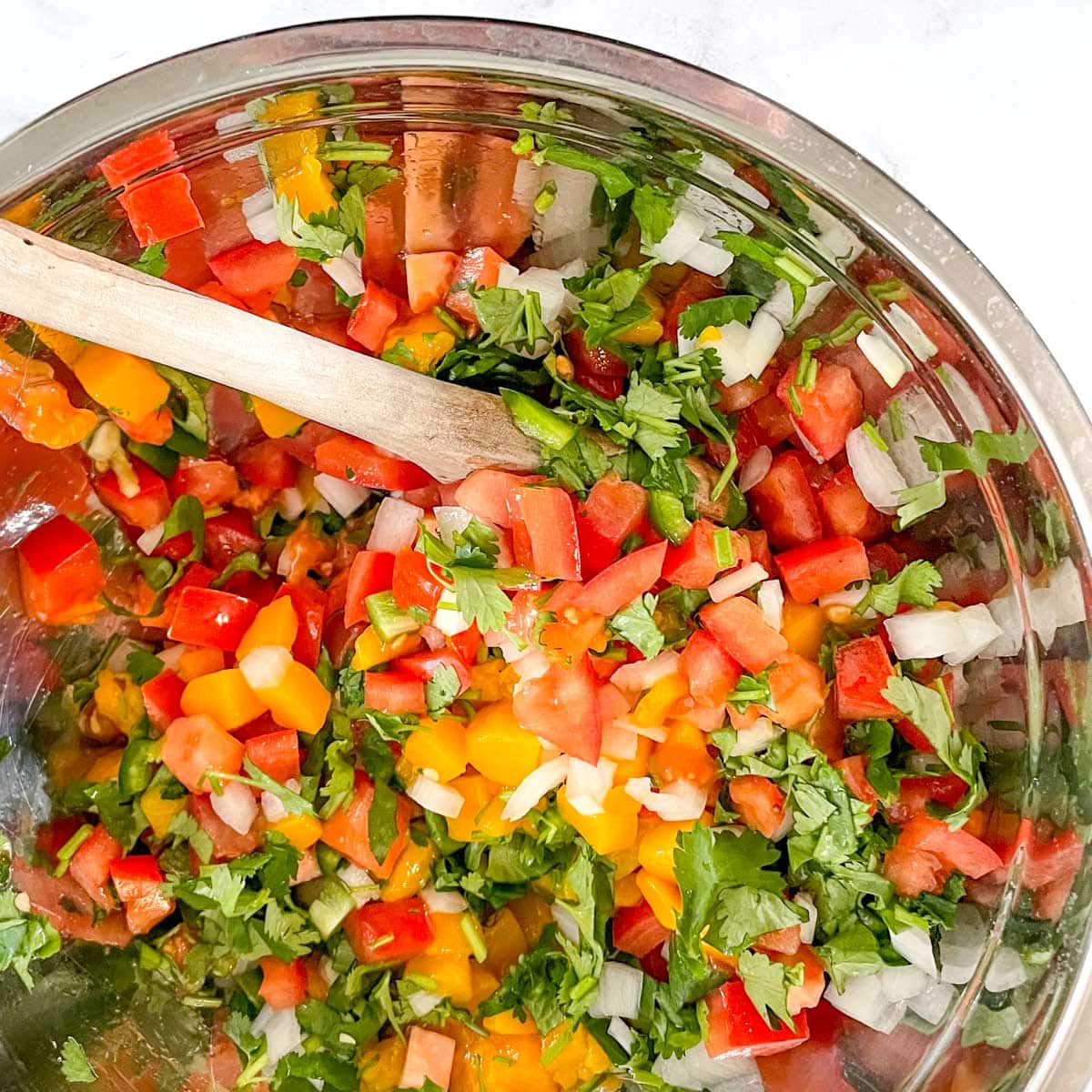 The ingredients for mango pico de gallo are stirred in a silver bowl.