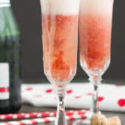 Two strawberry fizz cocktails sit beside a bottle of champagne.