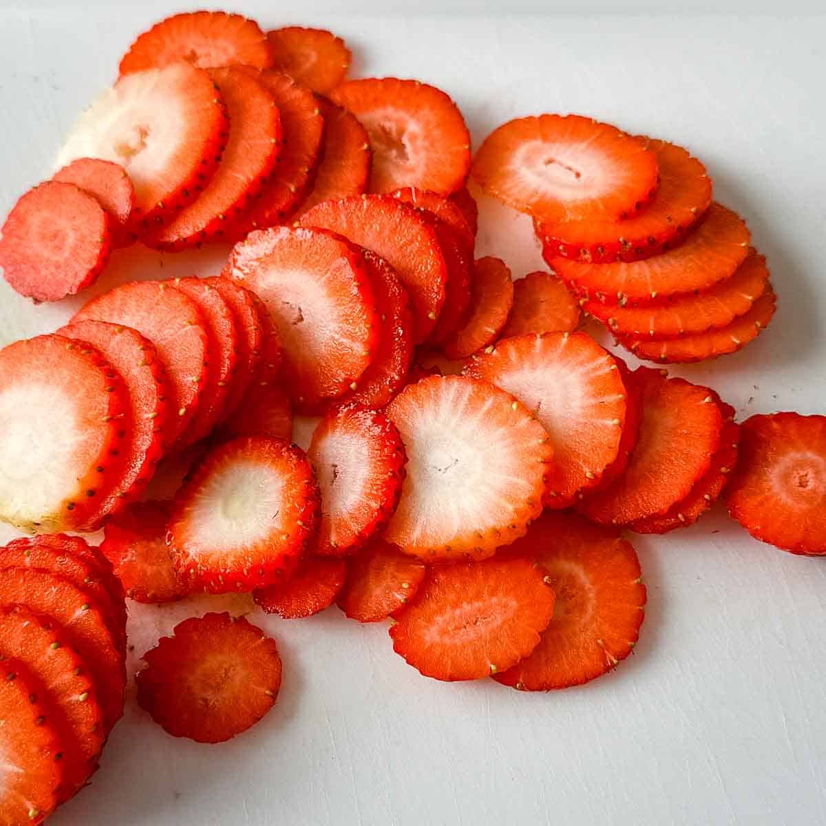 Sliced strawberries sit on a white cutting board.