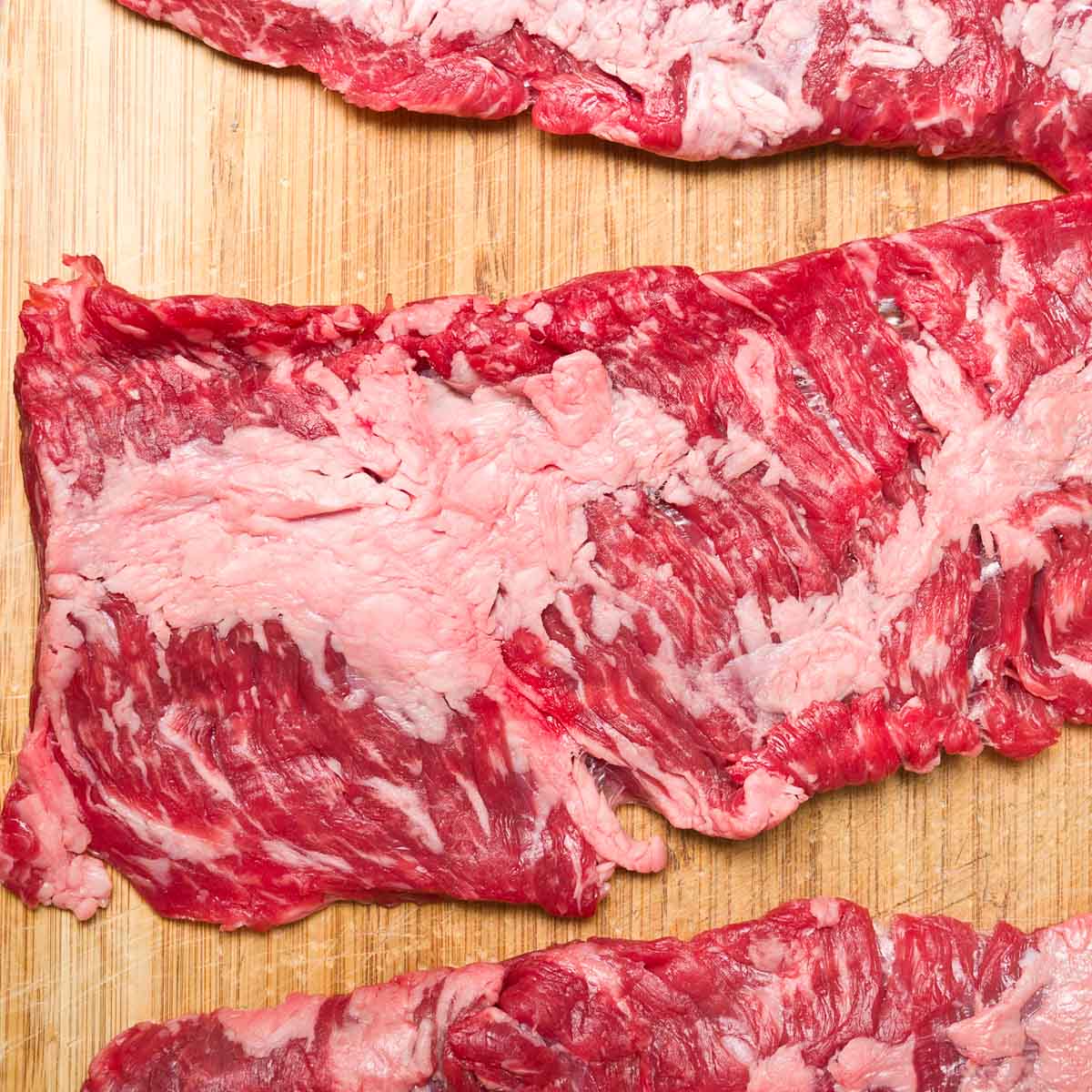 Skirt steak is shown on a wooden cutting board.