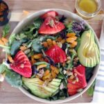 Strawberries, apricots, pistachios and avocado sit atop of bowl of greens.