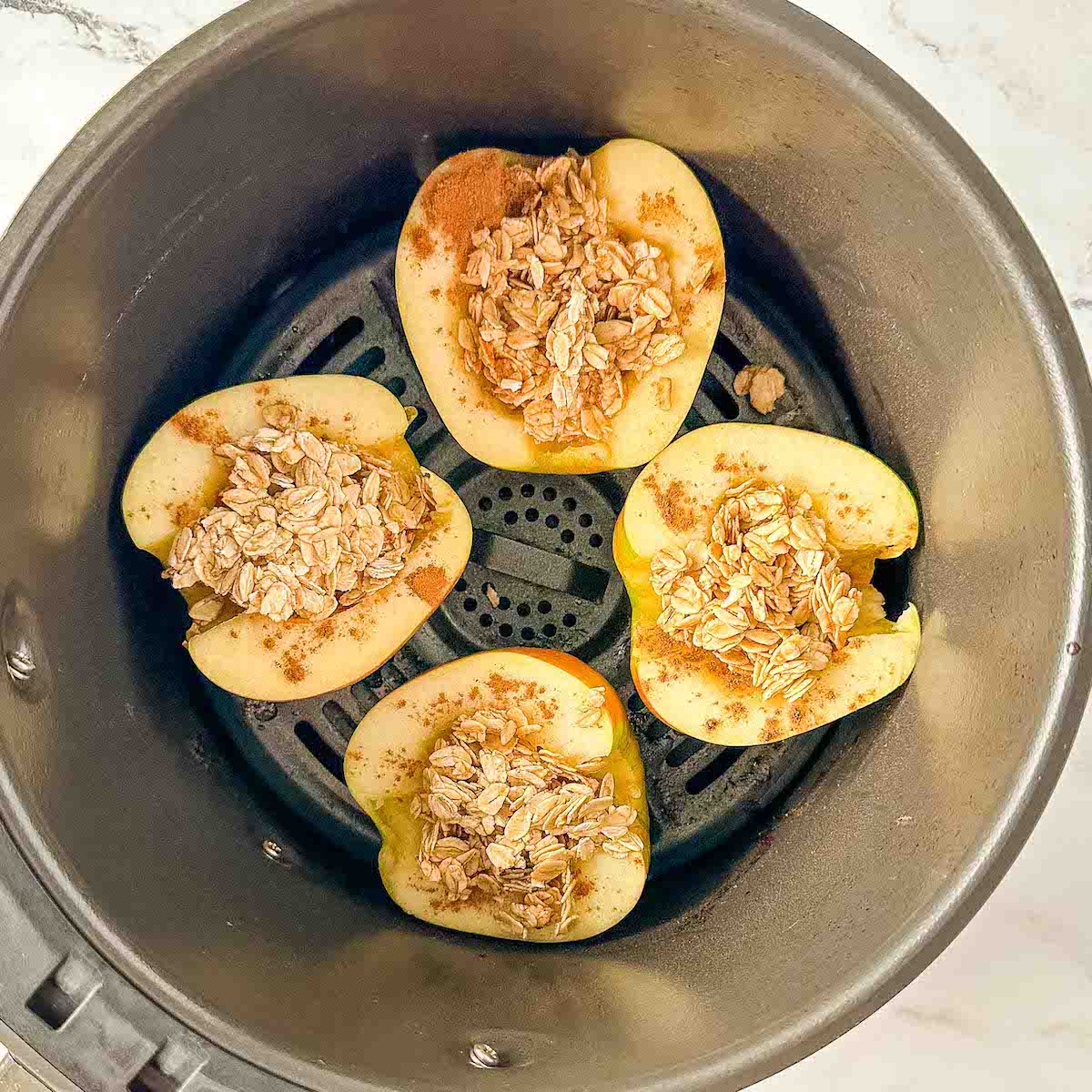 Apples filled with oat, cinnamon, maple mixture in an air fryer basket.