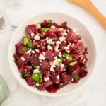 Beet salad sits in a white dish on a white counter.