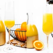 Two mimosas sit in front of a pitcher of orange juice and a bowl of oranges.