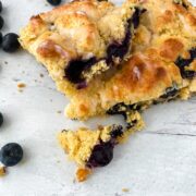 Blueberry lemon scones sit on a white wooden backdrop with blueberries surrounding them.