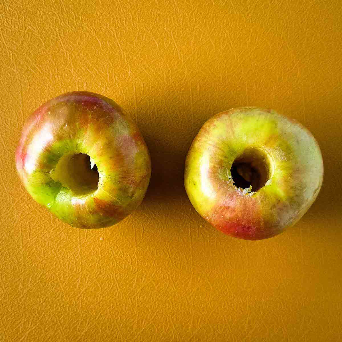 Cored apples sit on a yellow cutting board.