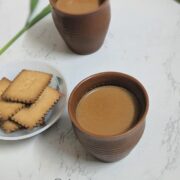 Two cups of lemongrass tea sit on a white marble counter with a plate of cookies.