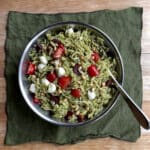 Orzo pesto salad is shown in a blue bowl over a green linen.