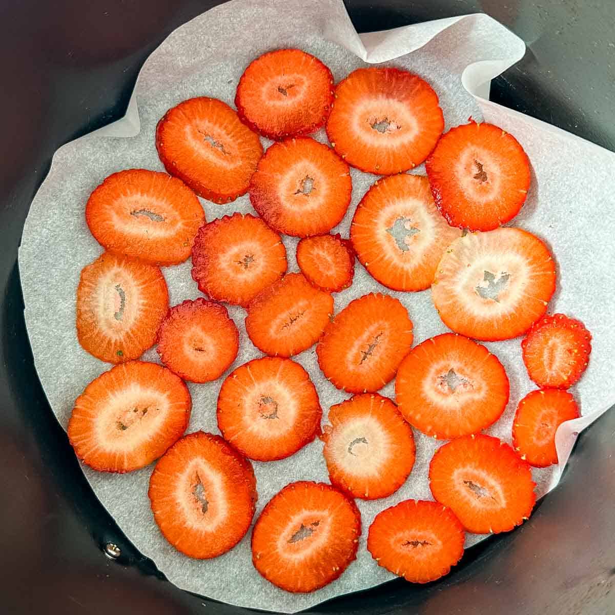 Sliced strawberries arranged in a single layer on parchment paper in an air fryer basket.