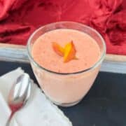 A strawberry peach smoothie is garnished with peach slices.