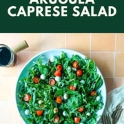Arugula caprese salad on a blue plate is shown with the words Arugula Caprese Salad and the URL www.twoclovesitchen.com.