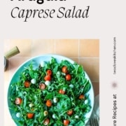 Arugula caprese salad on a blue plate is shown with the words Arugula Caprese Salad and the URL www.twoclovesitchen.com.