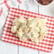 Potato salad sits on a white and red gingham plate.