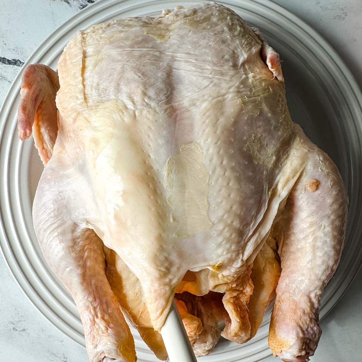 A small spatula is used to smear orange zest and butter under the skin of a whole raw chicken.