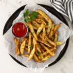 French fries sit on a piece of parchment paper on a black plate.