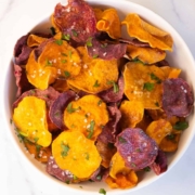 Multicolored air fryer sweet potato chips in a white bowl topped with salt.