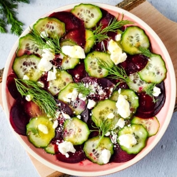 beet cucumber salad with feta and dill in a pink dish.