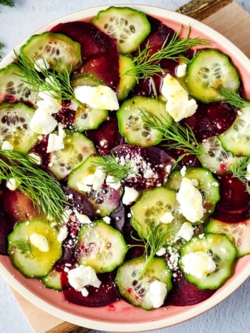beet cucumber salad with feta and dill in a pink dish.