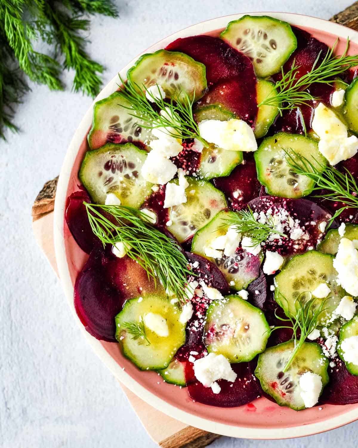 beet cucumber salad is shown on a pink plate with a wood cutting board and dill.