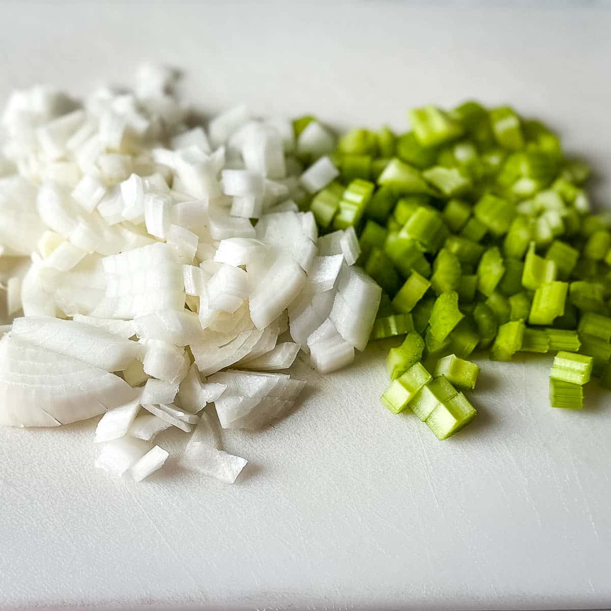 Finely diced onion and celery on a white cutting board.