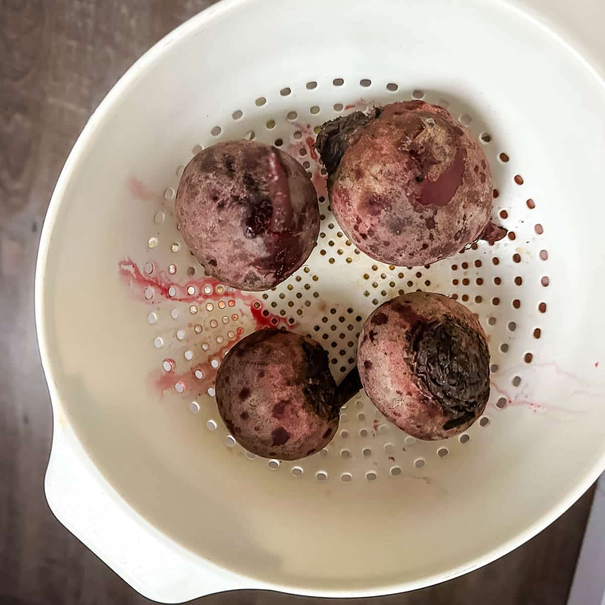boiled beets sit in a white colander.
