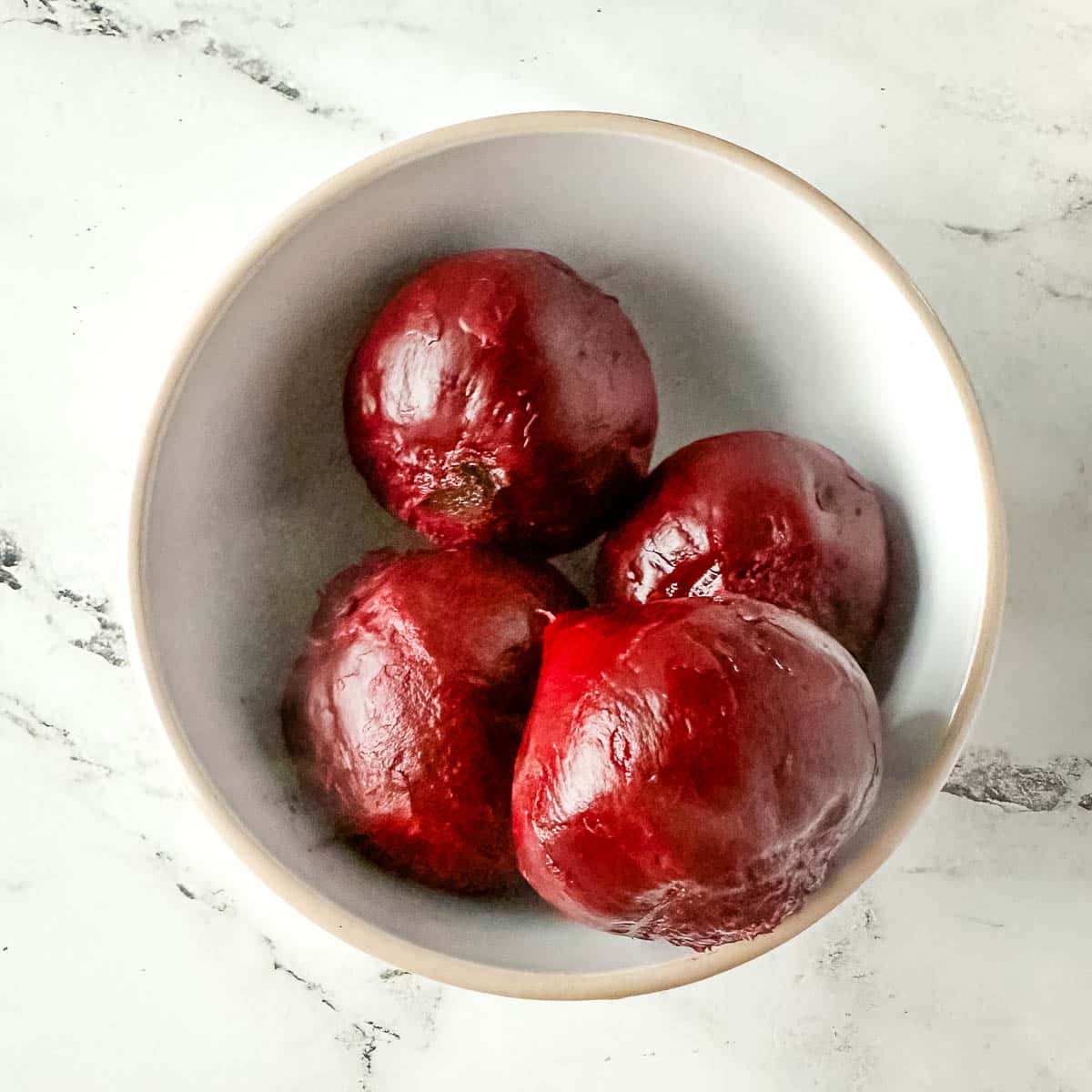 cooked beets with their skin removed in a white bowl.