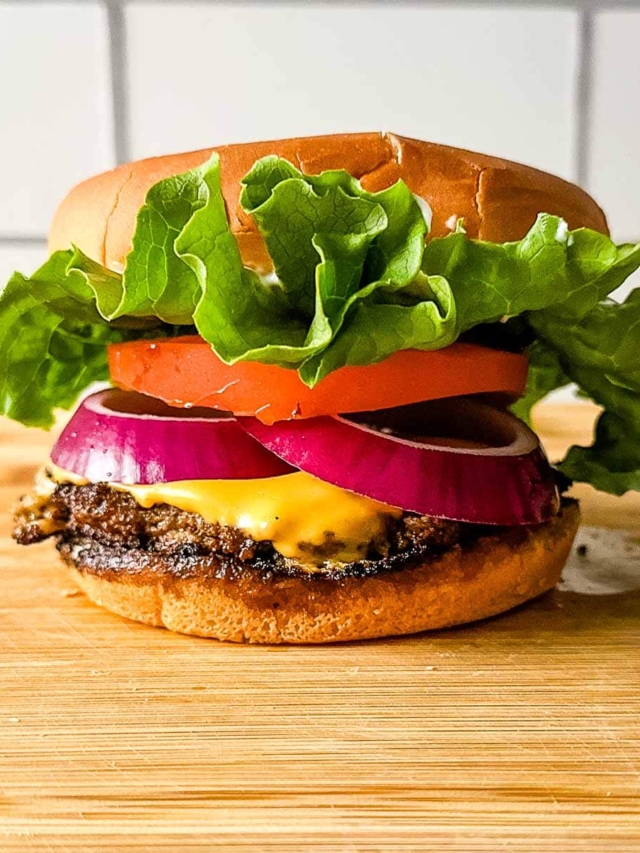 A turkey smash burger on a wooden cutting board in front of subway tile.