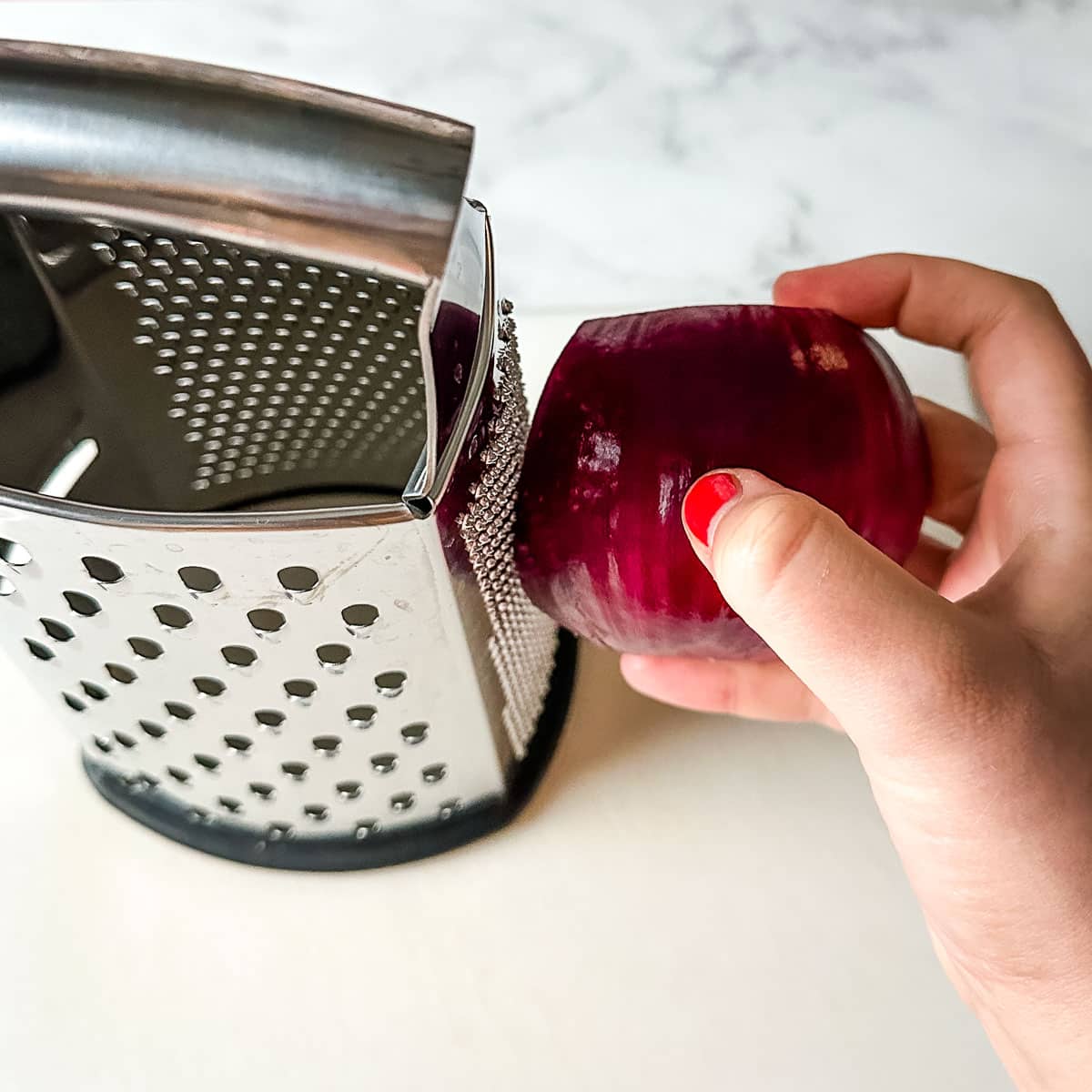 A red onion is grated on a box grater.
