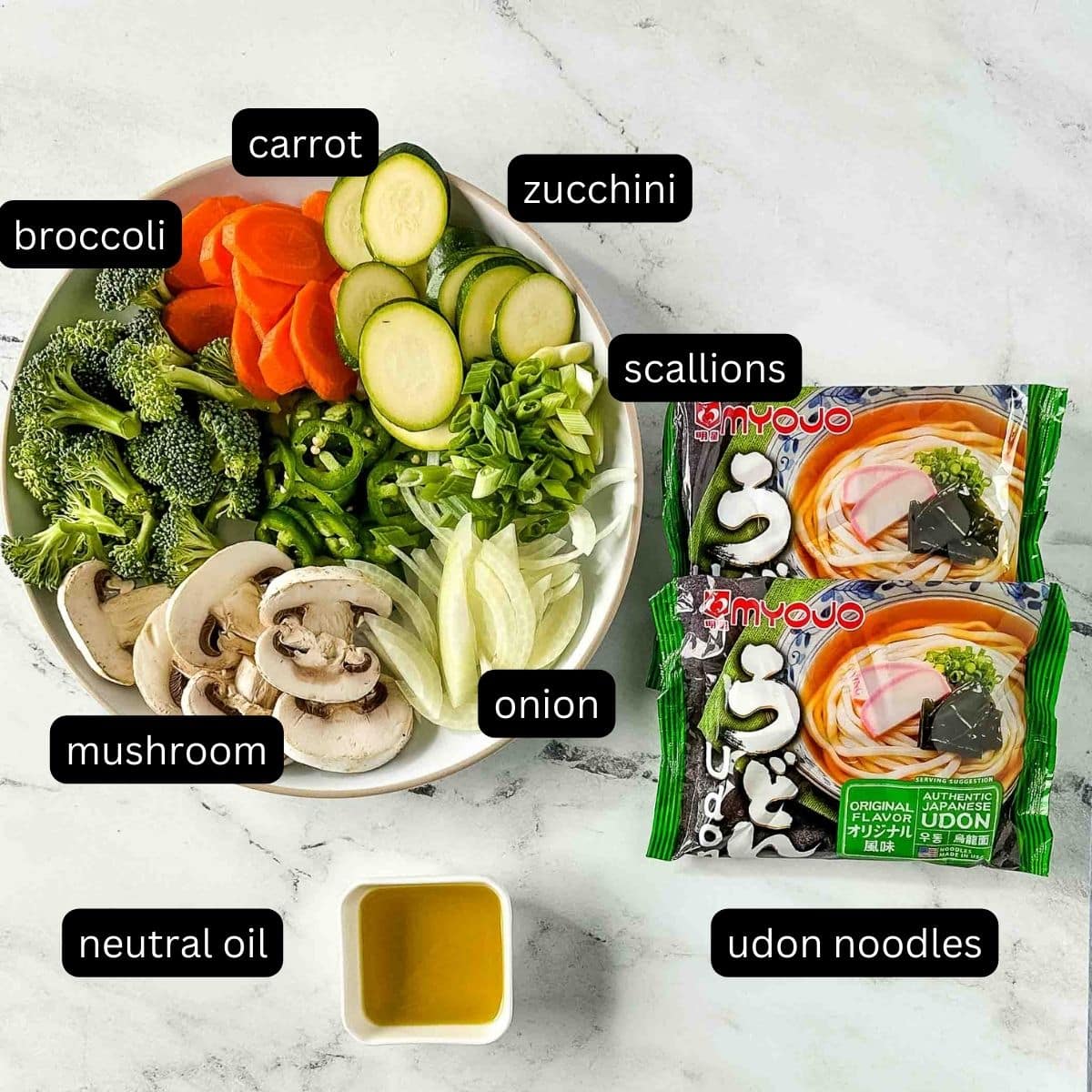 The labeled ingredients for vegetable yaki udon sit on a white marble counter.