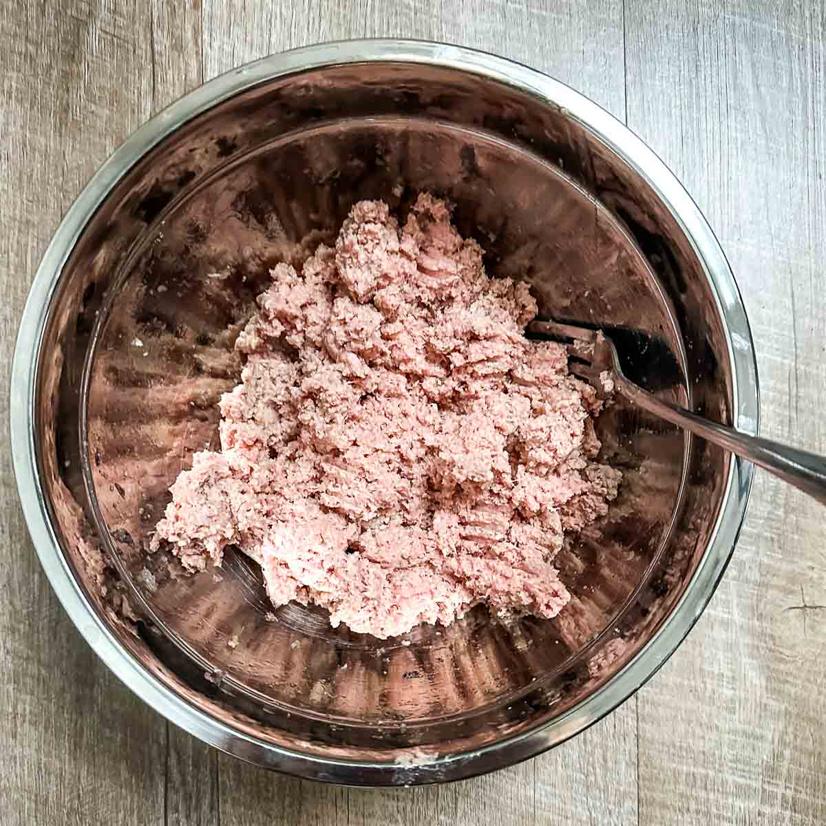ground turkey, salt, pepper, grated onion, and Worcestershire are mixed in a stainless steel bowl.