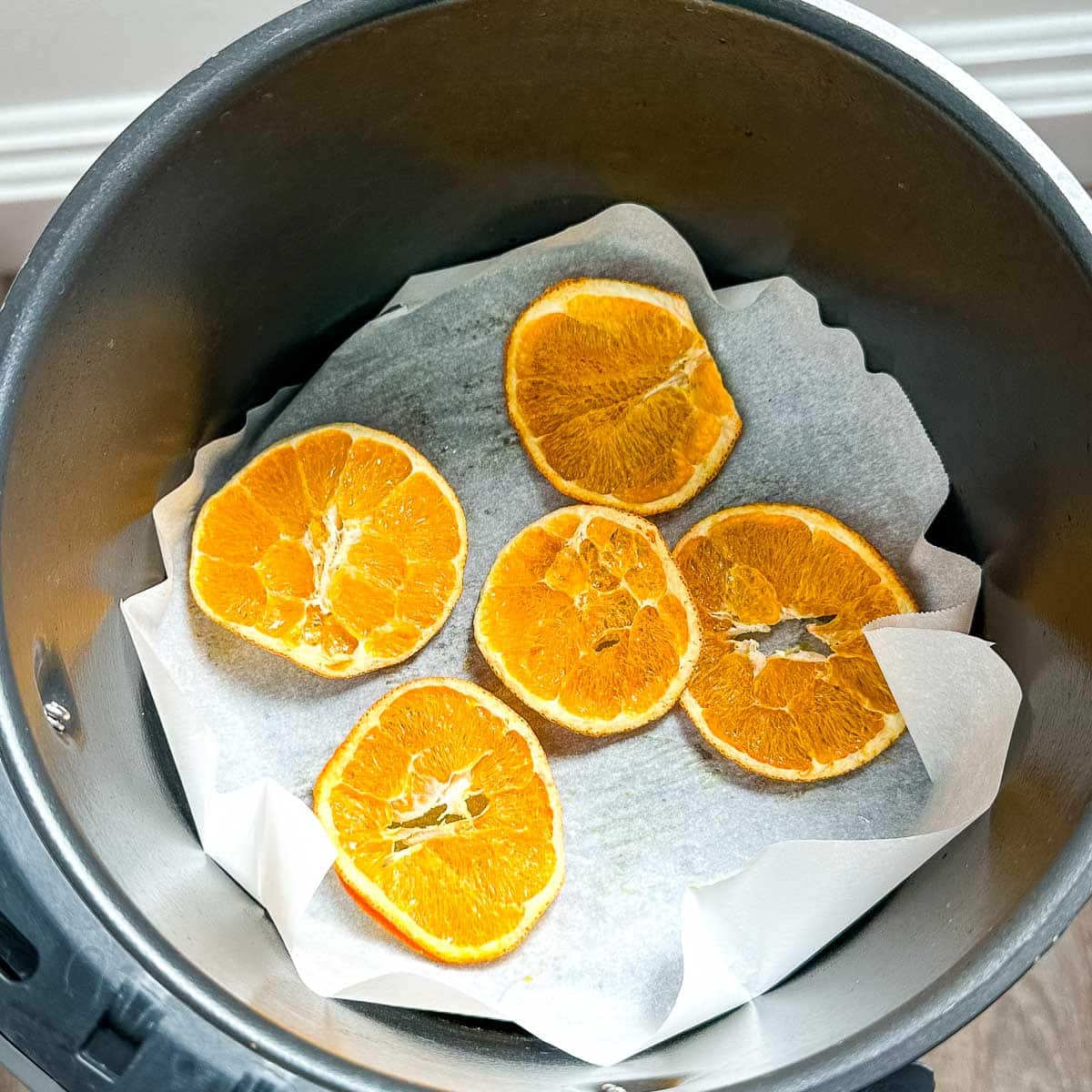 Dehydrated orange slices are shown in air fryer basket on parchment paper.