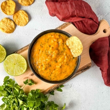 Roasted mango habanero salsa on a wooden cutting board surrounded by lime and cilantro.