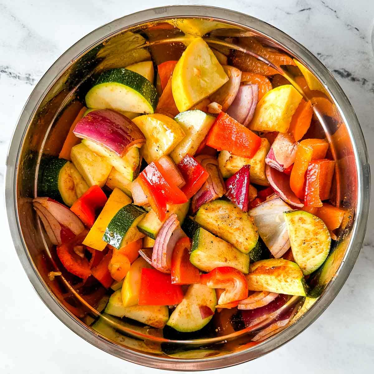 Cut vegetables in a stainless steel bowl seasoned with salt, pepper, cayenne, and olive oil.
