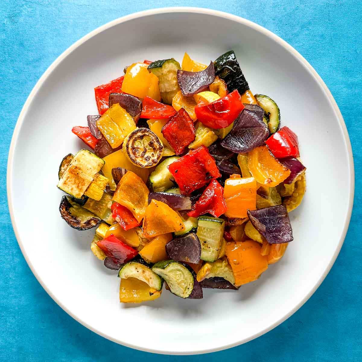 Spicy roasted vegetables on a white plate on a blue background.