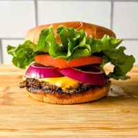 A turkey smash burger on a wooden cutting board in front of subway tile.