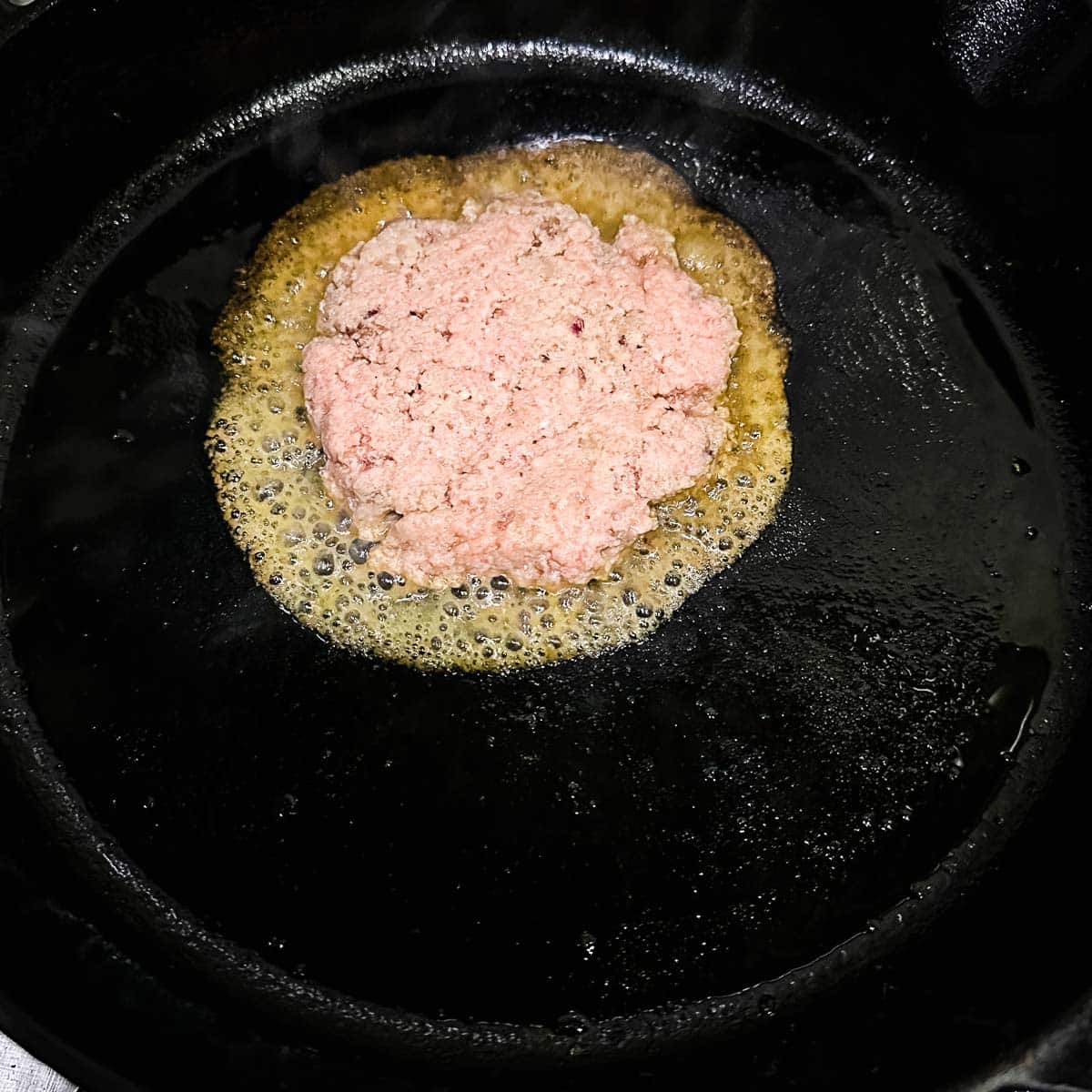 Turkey burger cooking in a cast iron pan.