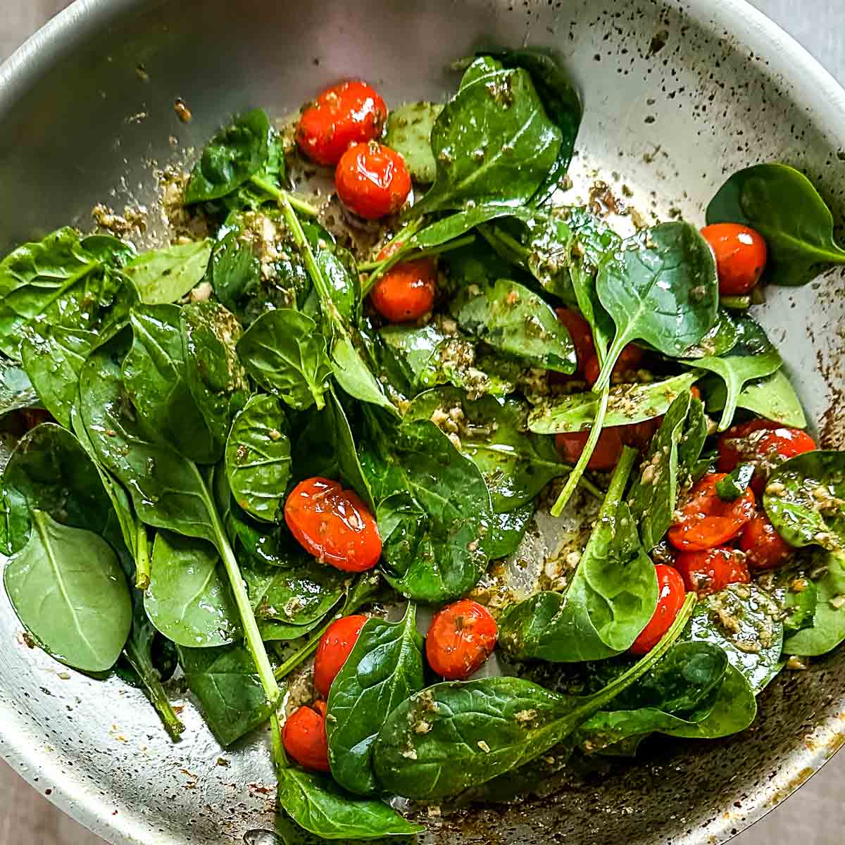 Spinach and tuna is mixed in with tomatoes, pesto, garlic, and olive oil in a pan.