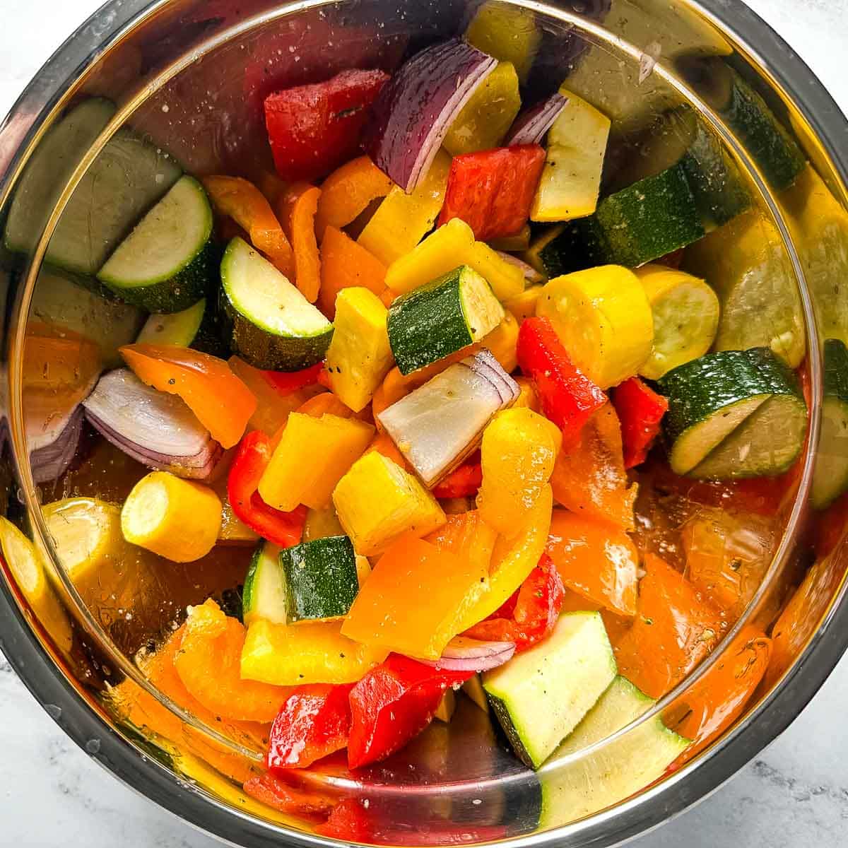 Cut vegetables tossed with olive oil and seasonings in a stainless steel bowl.
