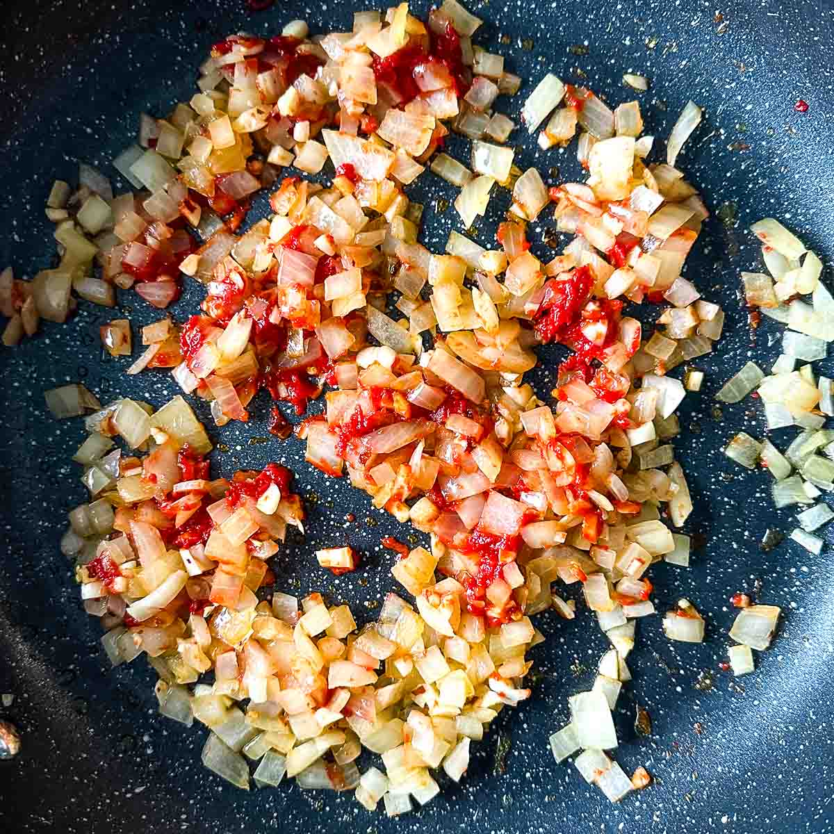 tomato paste is added to the frying pan with sweated onion, garlic, and chili flakes.