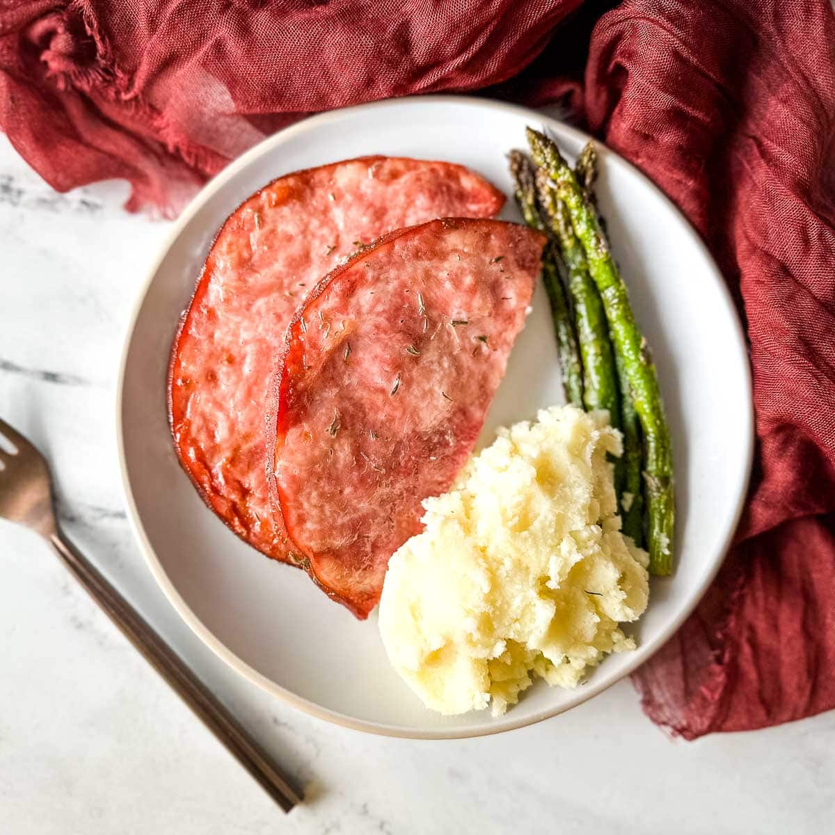 air fryer ham steak with mashed potatoes and asparagus on a white plate.