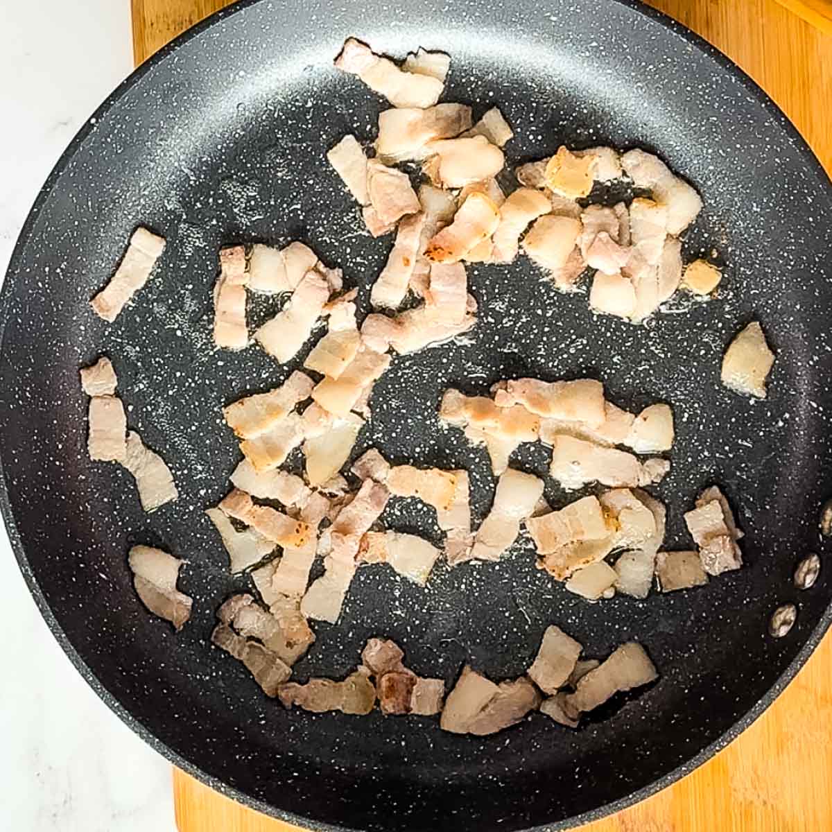 chopped bacon cooking in a pan.