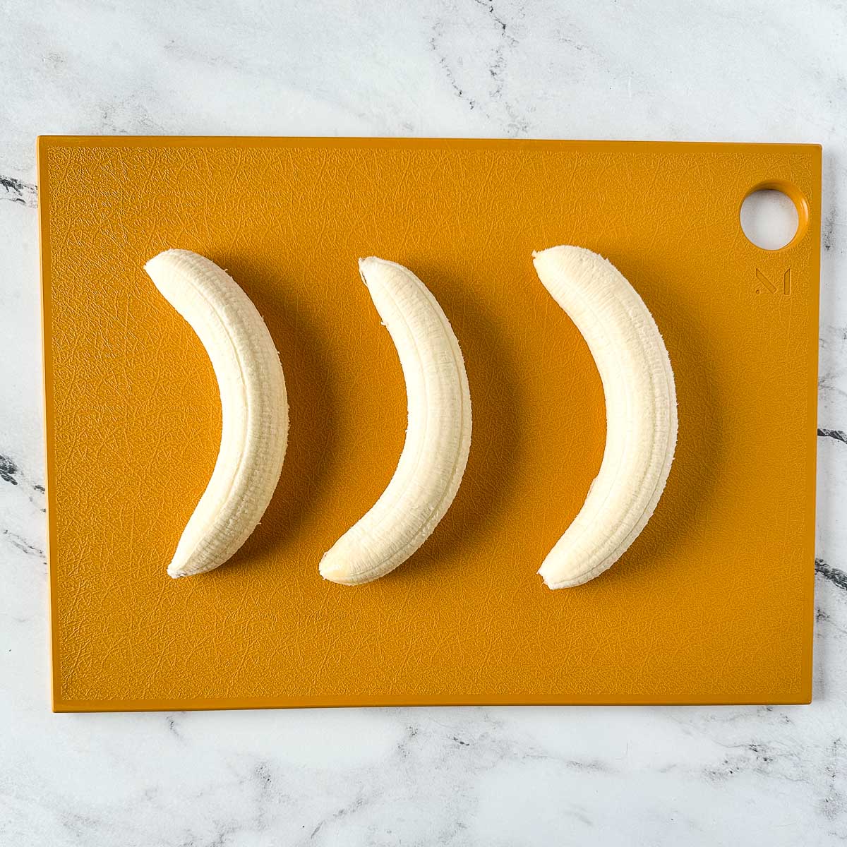 three peeled bananas on a yellow cutting board.