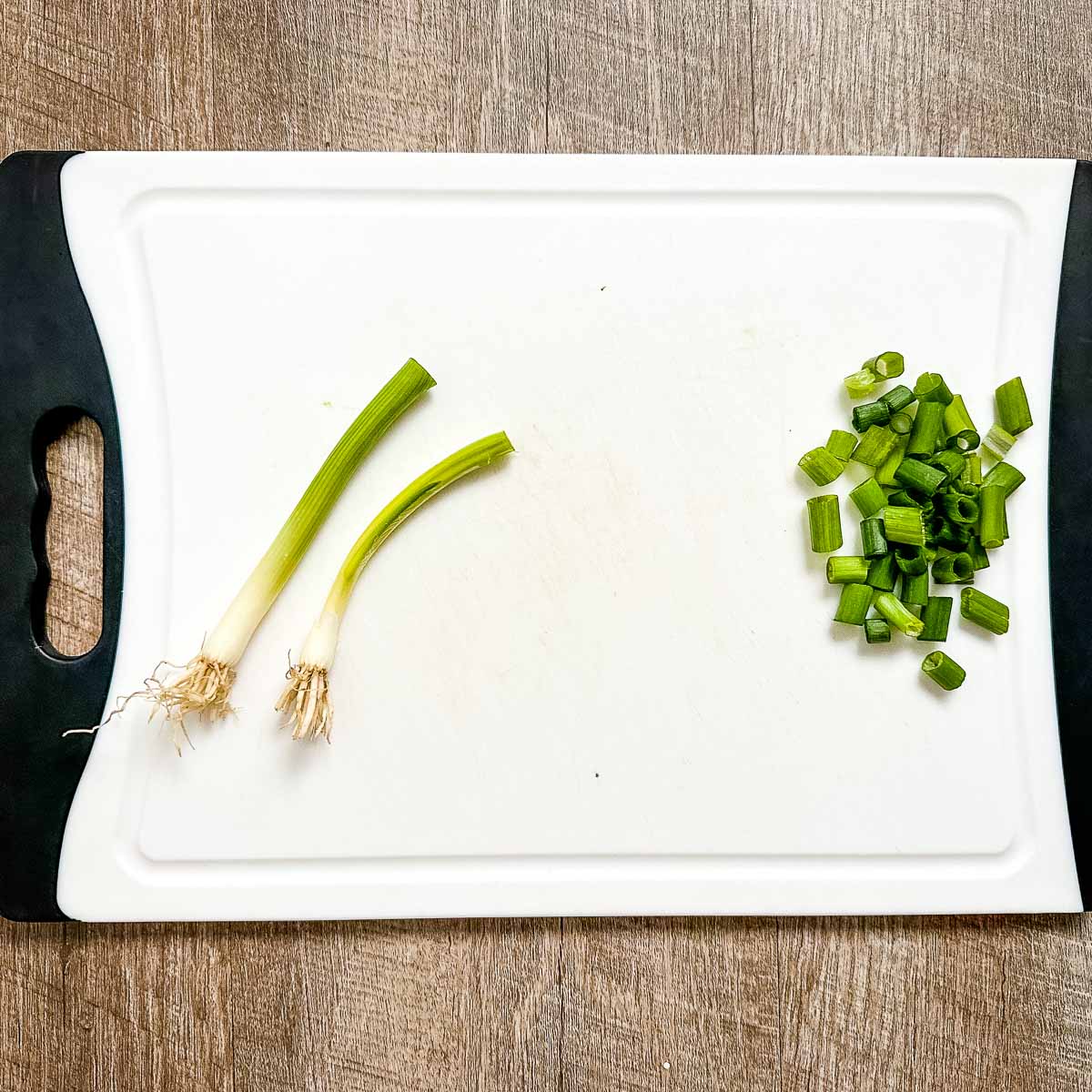 Two scallions are in the process of being chopped on a white cutting board.