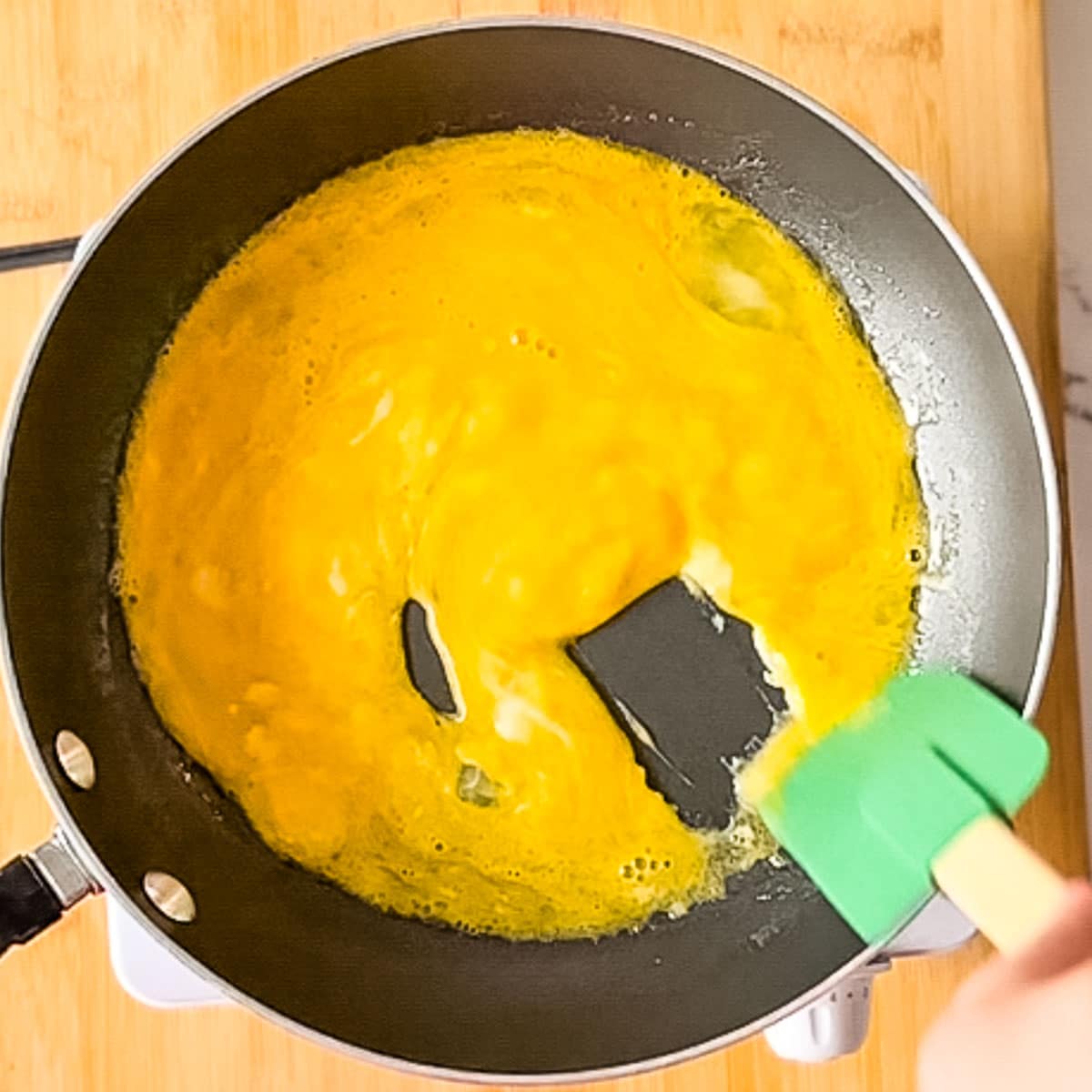 a green rubber spatula forms small curds in scrambled eggs as they cook.
