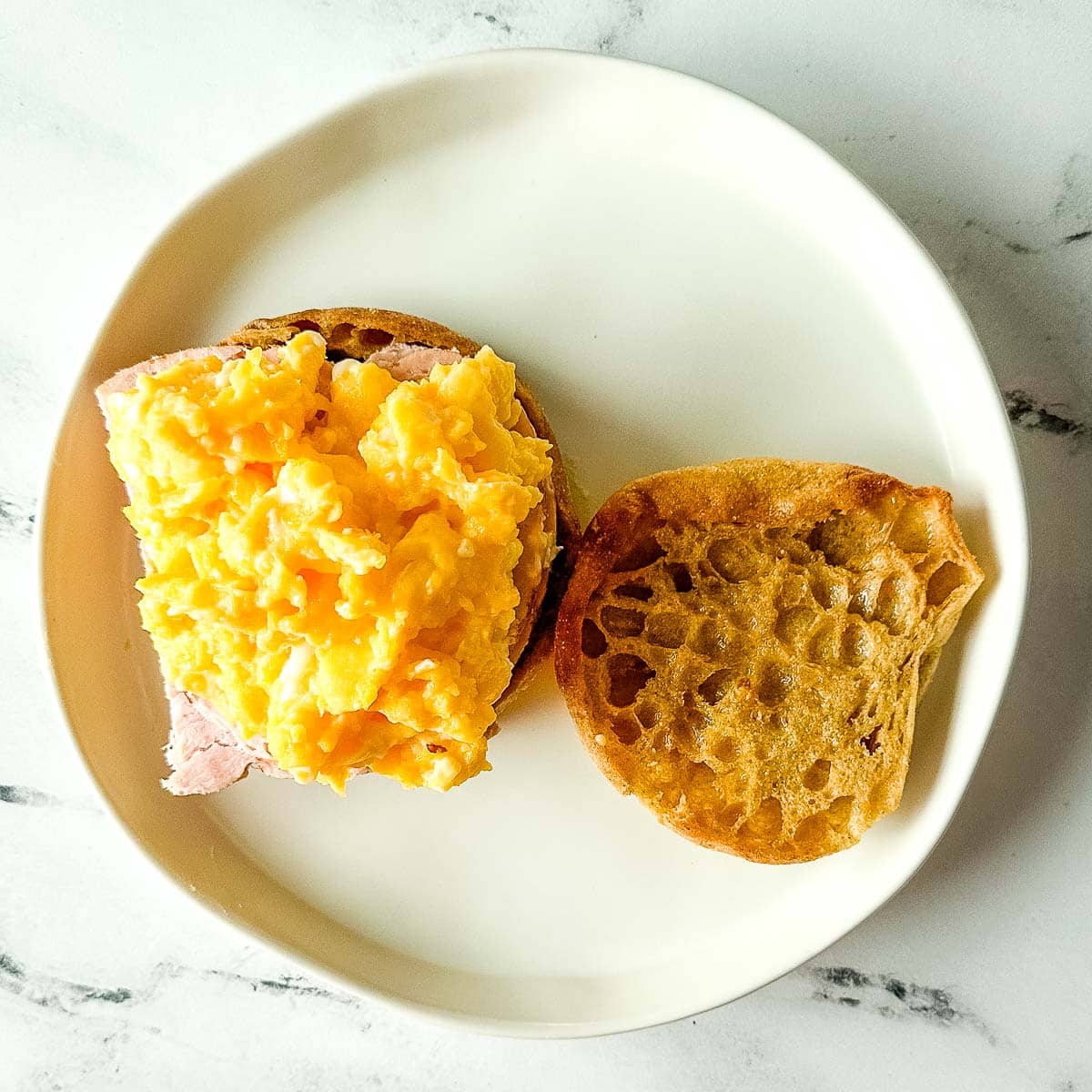 Toasted Englished muffin with turkey and scrambled eggs layered on top.